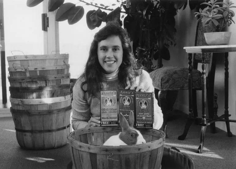 Annie Withey holding 3 boxes of Annie's Mac and Cheese. Her pet rabbit sits in a basket in front of her.