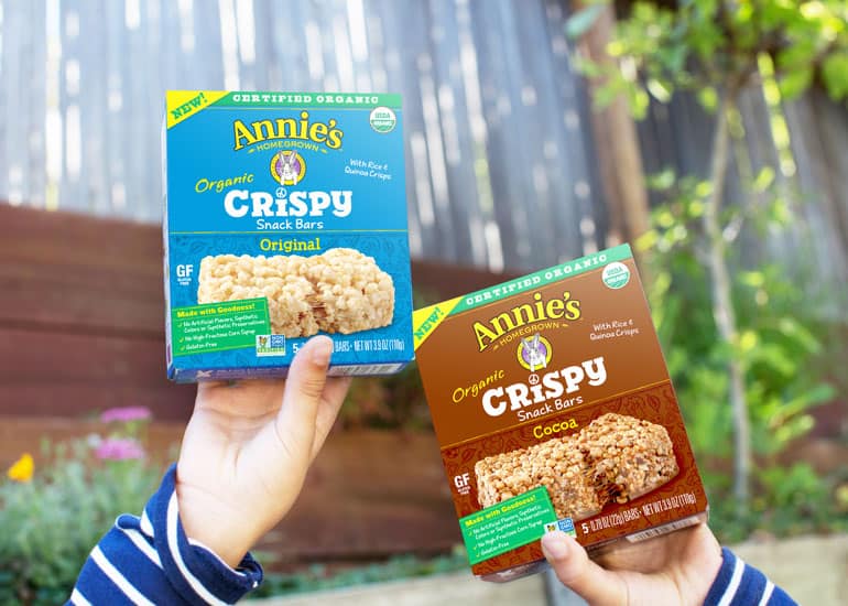 Child's hands showing two boxes of Annie's Crispy Snack Bars in Original and in Cocoa in each hand, front of box