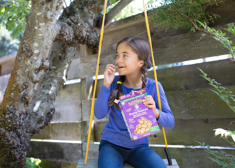 A child outside on a swing eating Annie's Bunny Grahams in Chocolate Chip