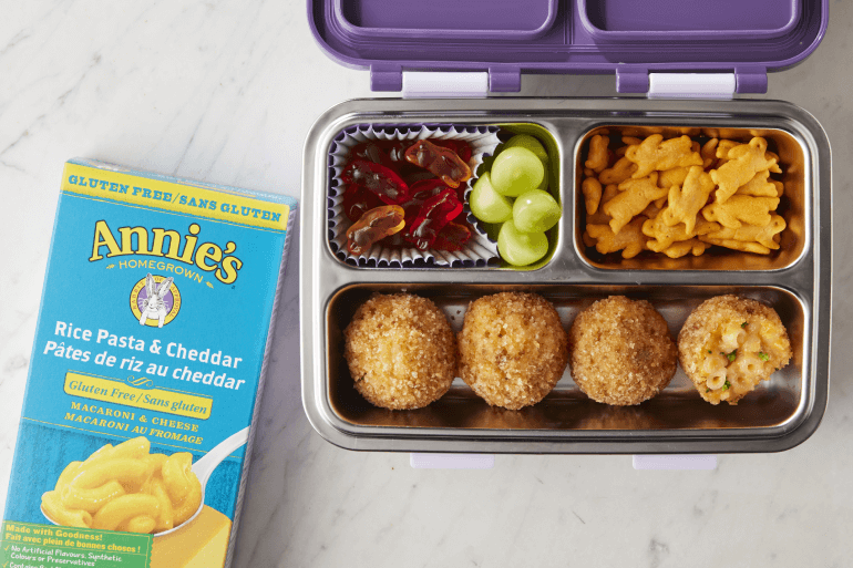 Annie's Rice Pasta & Cheddar, front of box next to a lunch box with prepared recipe of Gluten Free Lunch Box Broccoli Cheddar bites