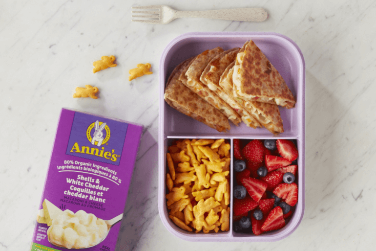 Annie’s Shells & White Cheddar, front of box next to a bento box with prepared recipe of Hot Dog Bento Box Quesadillas